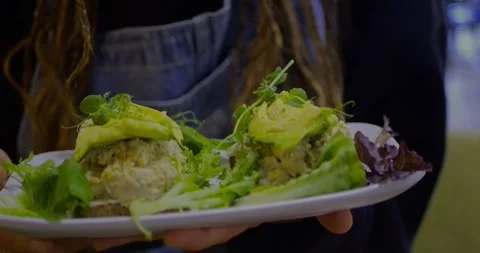 Plate held with both hands featuring two slices of avocado toast... Stock Footage 319880534