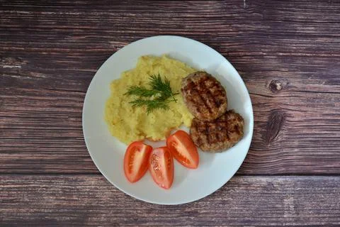 A plate of mashed potatoes with dill, two fried cutlets and ripe tomato sli.. Stock Photos