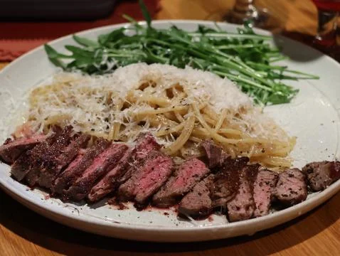 A plate of meat and pasta with a side of greens Stock Photos