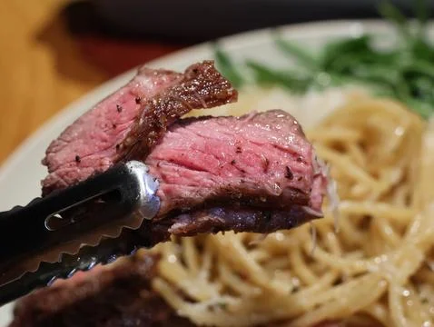 A plate of meat and pasta with a side of greens Stock Photos