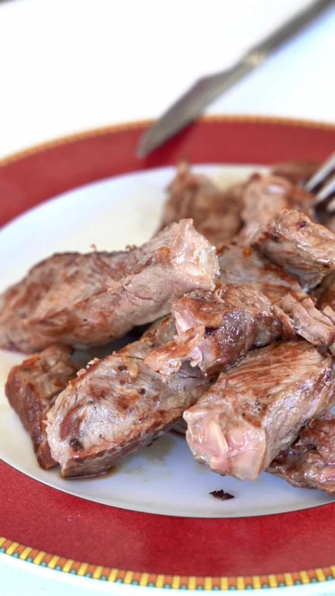 A plate of meat is on a red plate with a fork and knife on the table Stock Footage 327529405