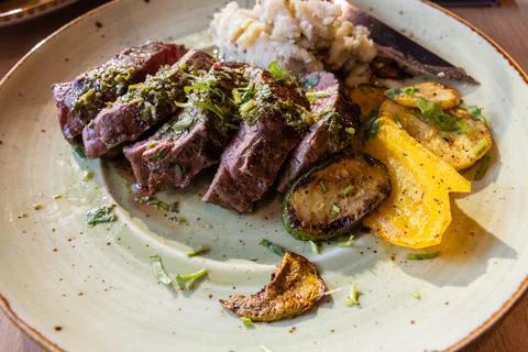 A plate of meat with a side of mashed potatoes and vegetables Stock Photos