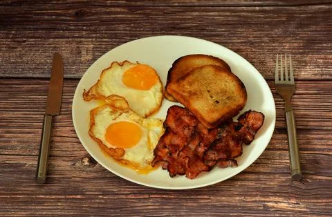 A plate of nutritious breakfast, two fried eggs, bacon and toast on a woode.. Stock Photos