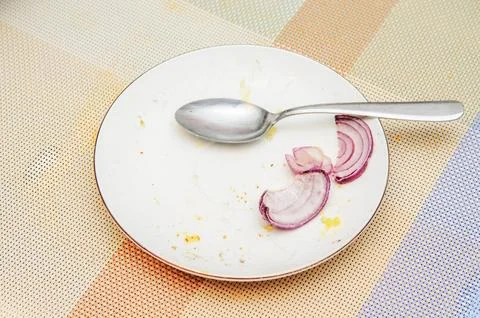 Plate with onion and spoon on a patterned tablecloth after a meal Stock Photos