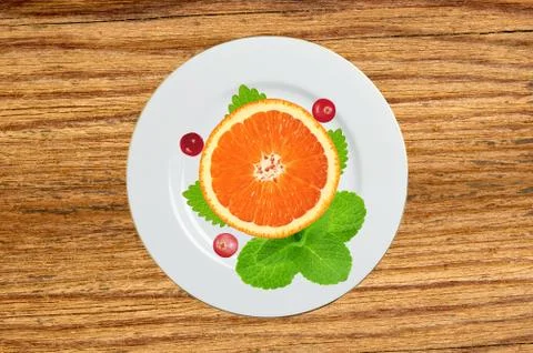 Plate with orange slice, mint herb and berry on wooden table Foto stock
