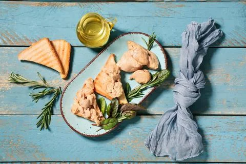 Plate with pieces of tasty cod liver and herbs on blue wooden background Stock Photos