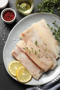 Plate with raw cod fish, microgreens, spices and lemon on dark table, flat la Stock Photos