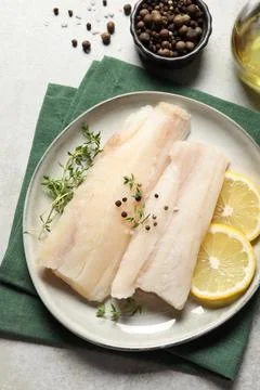 Plate with raw cod fish, spices, microgreens and lemon on grey table, flat la Stock Photos