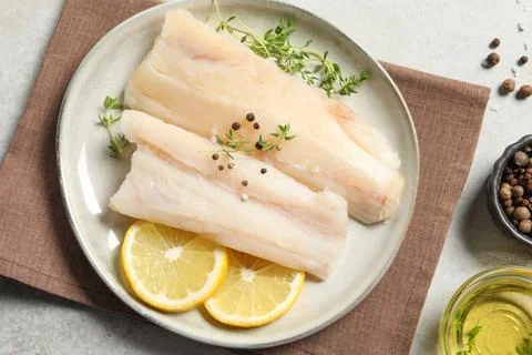 Plate with raw cod fish, spices, microgreens and lemon on grey table, flat la Stock Photos