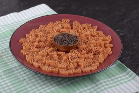 A plate of raw pasta in hearts shape with pepper on black table Stock Photos