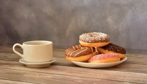 A plate with several donuts in multi-colored glaze and a cup of hot black c.. Stock Photos