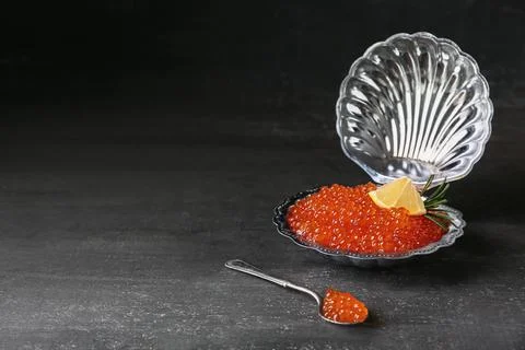 Plate in shape of seashell with delicious red caviar on dark table Stock Photos