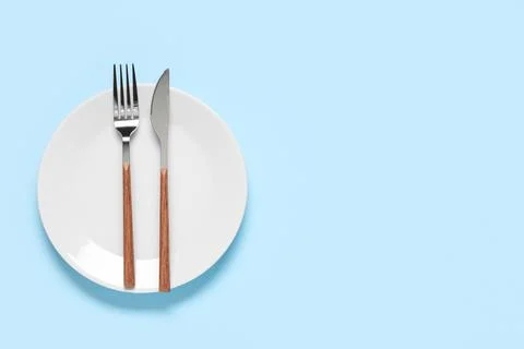 Plate with silver fork and knife on blue background Stock Photos