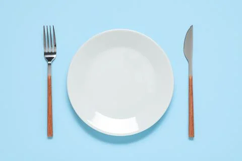 Plate with silver fork and knife on blue background Stock Photos