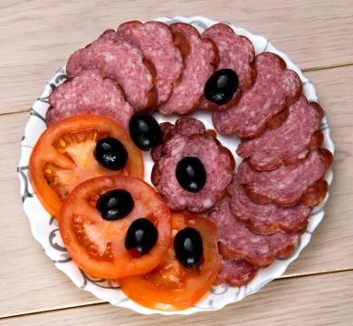 Plate of sliced sausage, tomato and olives on wooden table  background Stock Photos