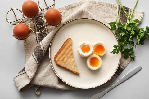 Plate with soft boiled eggs and slice of bread on grey background Stock Photos