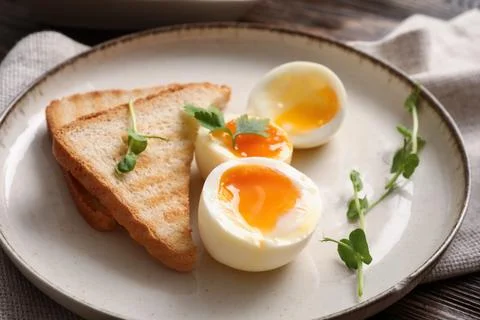 Plate with soft boiled eggs, micro green and slices of bread on wooden backgr Stock Photos