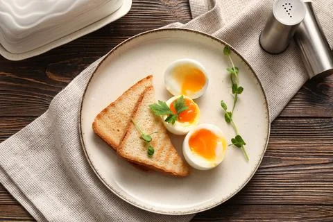 Plate with soft boiled eggs, micro green and slices of bread on wooden backgr Stock Photos