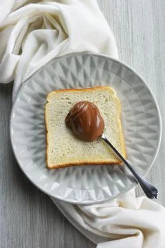 Plate with spoonful of hazelnut praline paste on slice of bread Stock Photos
