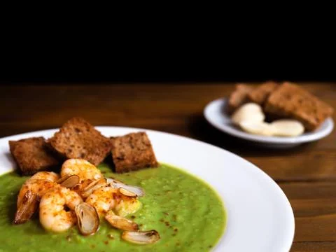 A plate of thick fresh green pea soup with prawns on a rustic wooden table wi Stock Photos