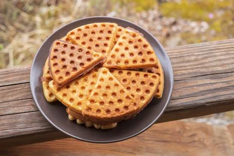 A plate of triangular sweet waffles stands on the wooden railing of the gazeb Stock Photos