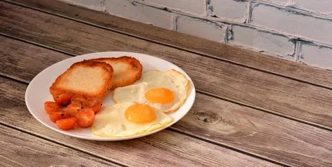 Plate with two fried eggs, cherry tomatoes and wheat bread croutons on wood.. Stock Photos