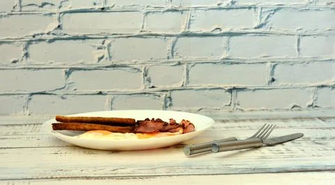 A plate with two fried eggs, crispy bacon slices and bread toast on a light.. Stock Photos