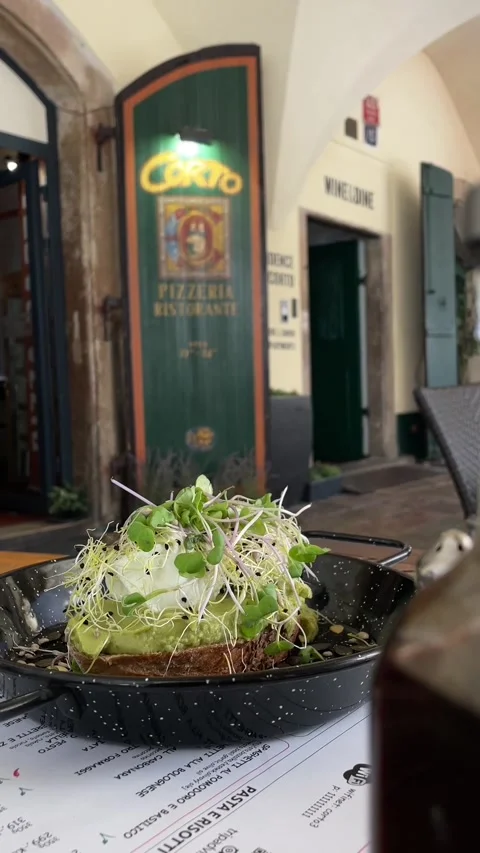 Plated avocado toast presented on rustic bistro table with blurred pizzeria Stock Footage 344584976