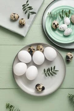 Plates with Easter eggs and eucalyptus branches on green wooden background Stock Photos