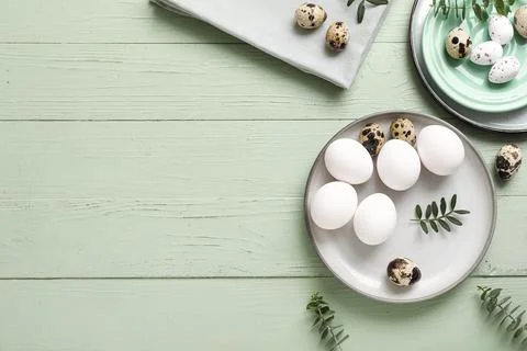 Plates with Easter eggs and eucalyptus branches on green wooden background Stock Photos