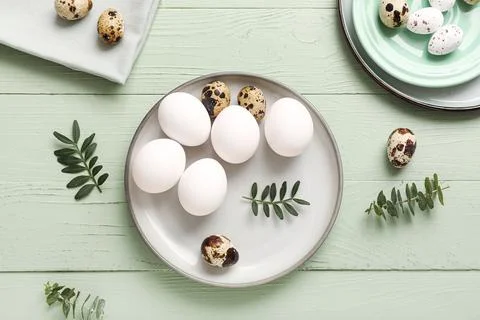 Plates with Easter eggs and eucalyptus branches on green wooden background Stock Photos