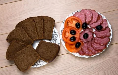 Plates of sliced black bread and sausage on wooden table Stock Photos