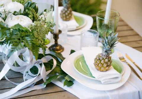 Plates on the table decorated with pineapples, candles and flowers, green and Stock Photos