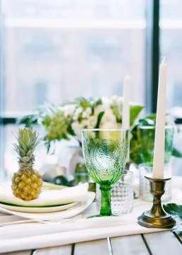 Plates on the table decorated with pineapples, candles and flowers, green and Stock Photos