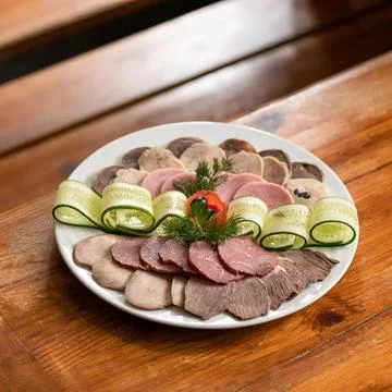 Platter with cold cuts, thin slices of meat, ham and cucumber rolls on wooden Stock Photos