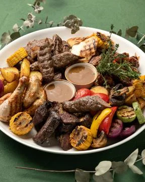 Platter with mixed grilled meat and vegetables on green background. Tasty lunch Stock Photos