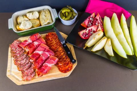 Platters of cured meats, fruit, bread and gherkins. Stock Photos