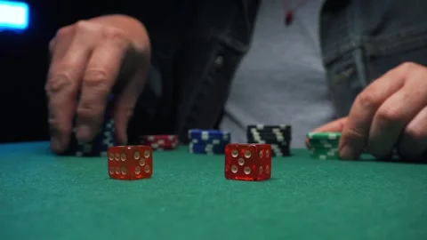 Player rolls dice and places poker chips on green felt table during a game night Stock Footage 335171536