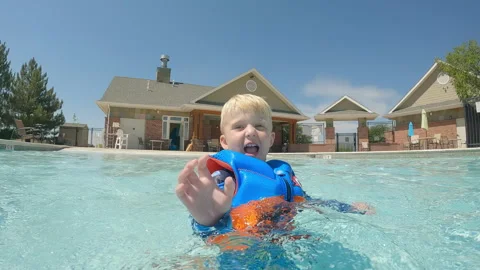 Playful 4 year old boy splashes water at camera with his hand, neighborhood pool 스톡 동영상 248081084