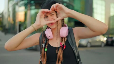 Playful adolescent making heart shape with hands winking outdoors. Zoomers Stock Footage 340479424