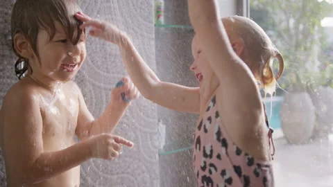 A playful boy washes under a shower stream while his sister waves her hands 스톡 동영상 296715251
