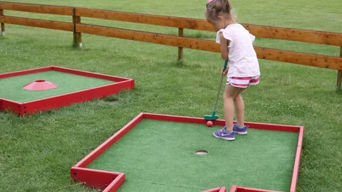 Playful childhood - little child girl enjoy play mini golf in park club Stock Footage