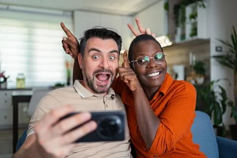 Playful couple taking a selfie making funny faces at home Stock Photos