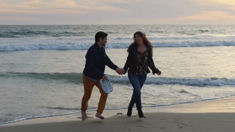 Playful Couple Wait For Wave To Get Close To Their Feet, They Run Away From It Video stock 90232297