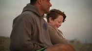 Playful Father And Son Sitting On Beach At Sunset Stock Footage