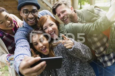 Playful friends with camera phone gesturing taking selfie Stock Photos
