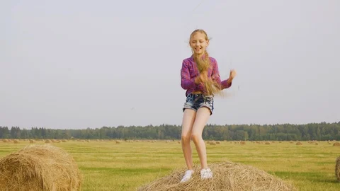 Playful girl dancing on hay stack with straw in hands at harvesting field Stock Footage 113344788