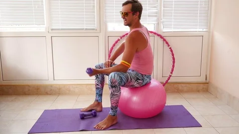 A playful handsome guy in a pink T-shirt and blue leggings is engaged in fitness Stock Footage 77696038