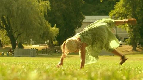 Playful little blonde girl performs handspring on a green park lawn on a sunny Stock Photos