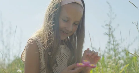Playful Little Girl Spinning a Spinner Sitting on Green Grass on Field Stock Footage